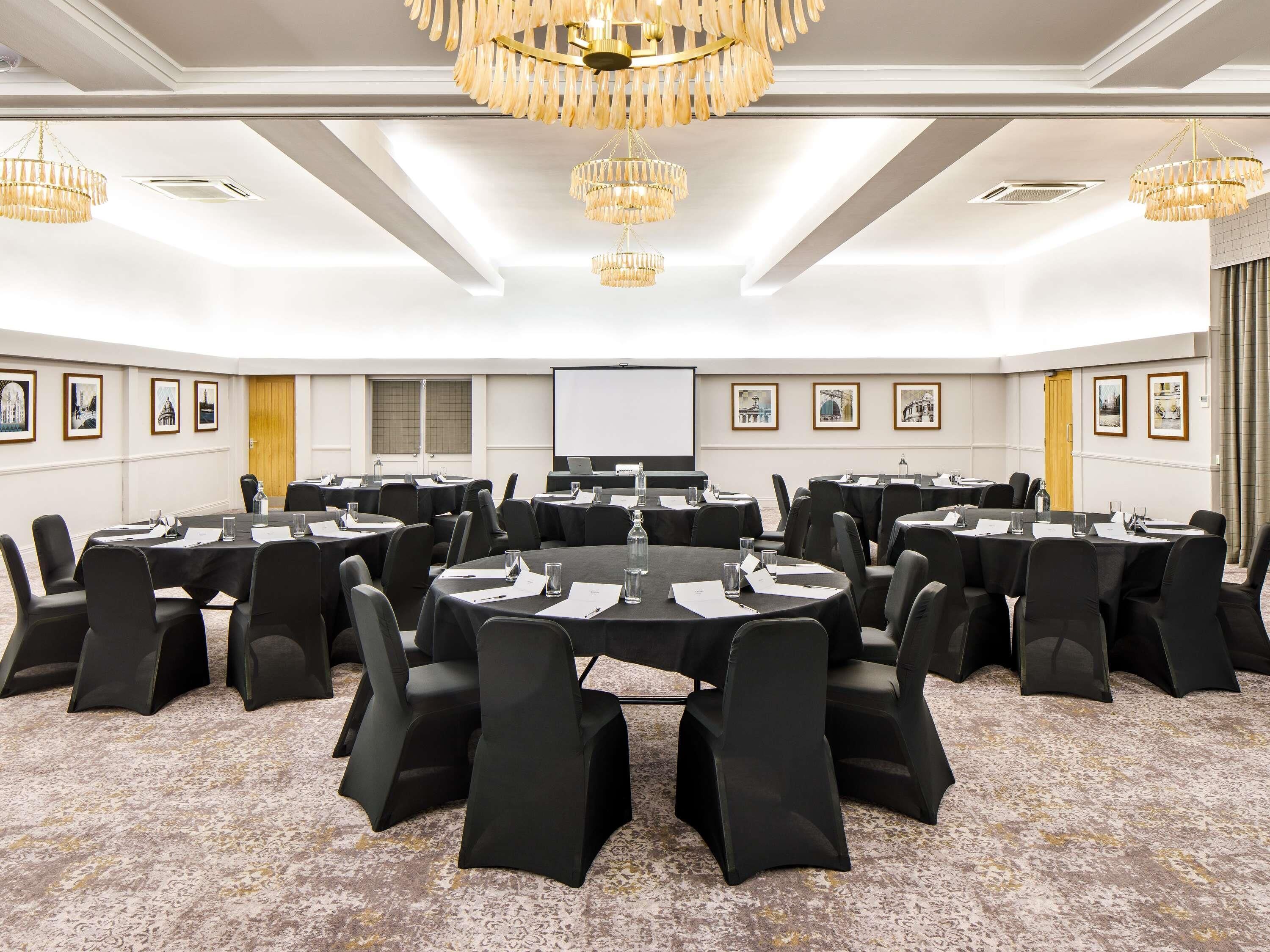 A conference room with round tables, black chairs, and chandeliers.