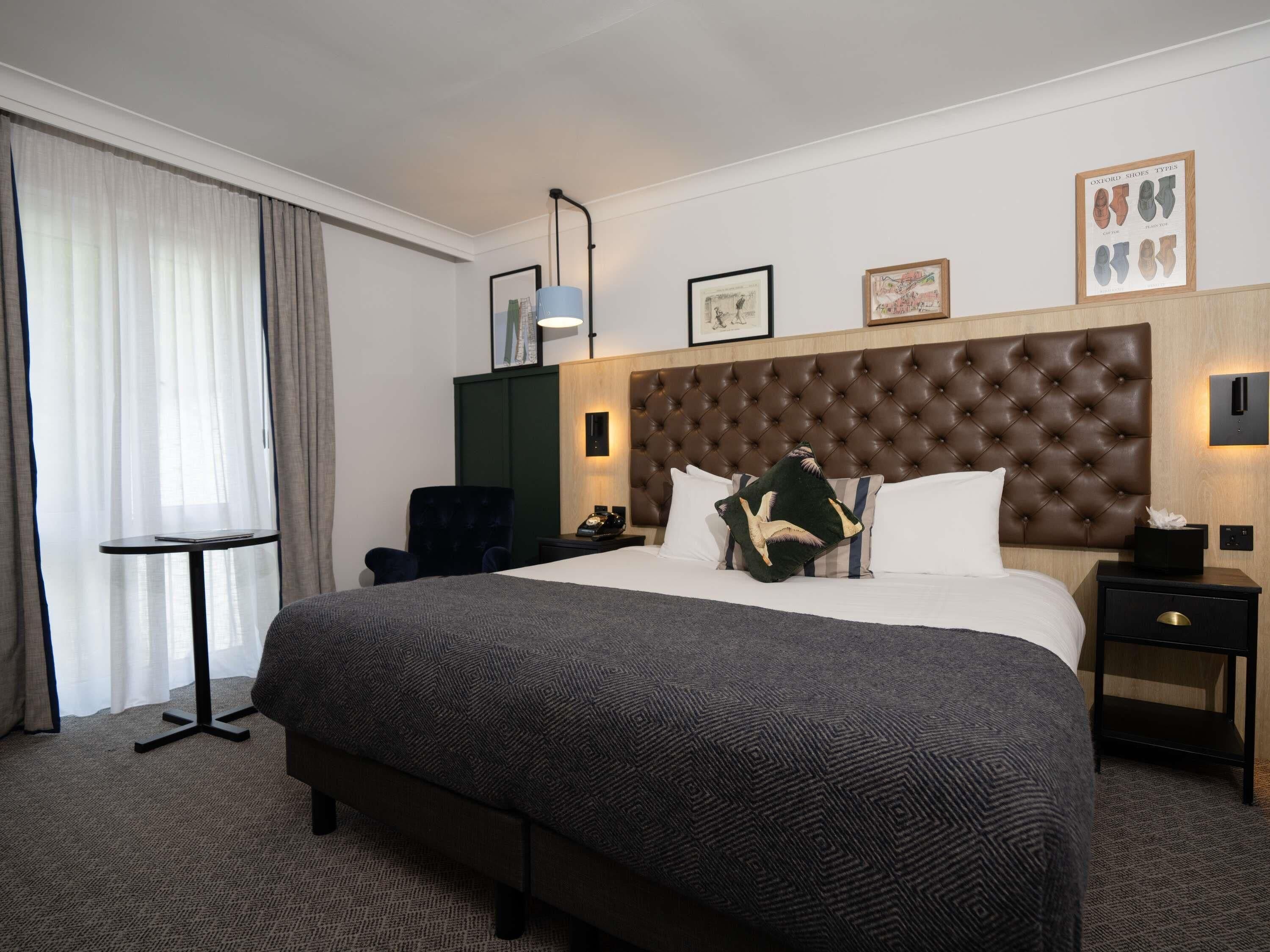 A hotel room with a large bed, a desk, a chair, a lamp, and a framed picture on the wall.