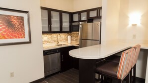 A modern kitchen with dark cabinets, stainless steel appliances, a white countertop, and a striped bar stool.