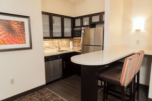 A modern kitchen with dark cabinets, stainless steel appliances, a white countertop, and a striped bar stool. - Staybridge Suites Indianapolis-Fishers by IHG (Indianapolis)