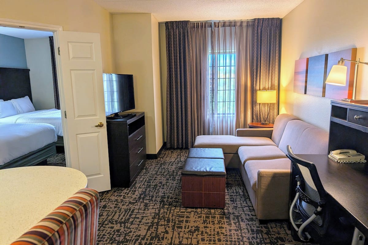 Une chambre d’hôtel avec deux lits, un canapé, un bureau avec une lampe, une télévision et une moquette à motifs.