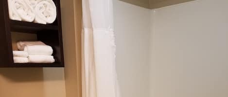 A bathroom with a toilet, a bathtub, and a shelf with rolled towels.