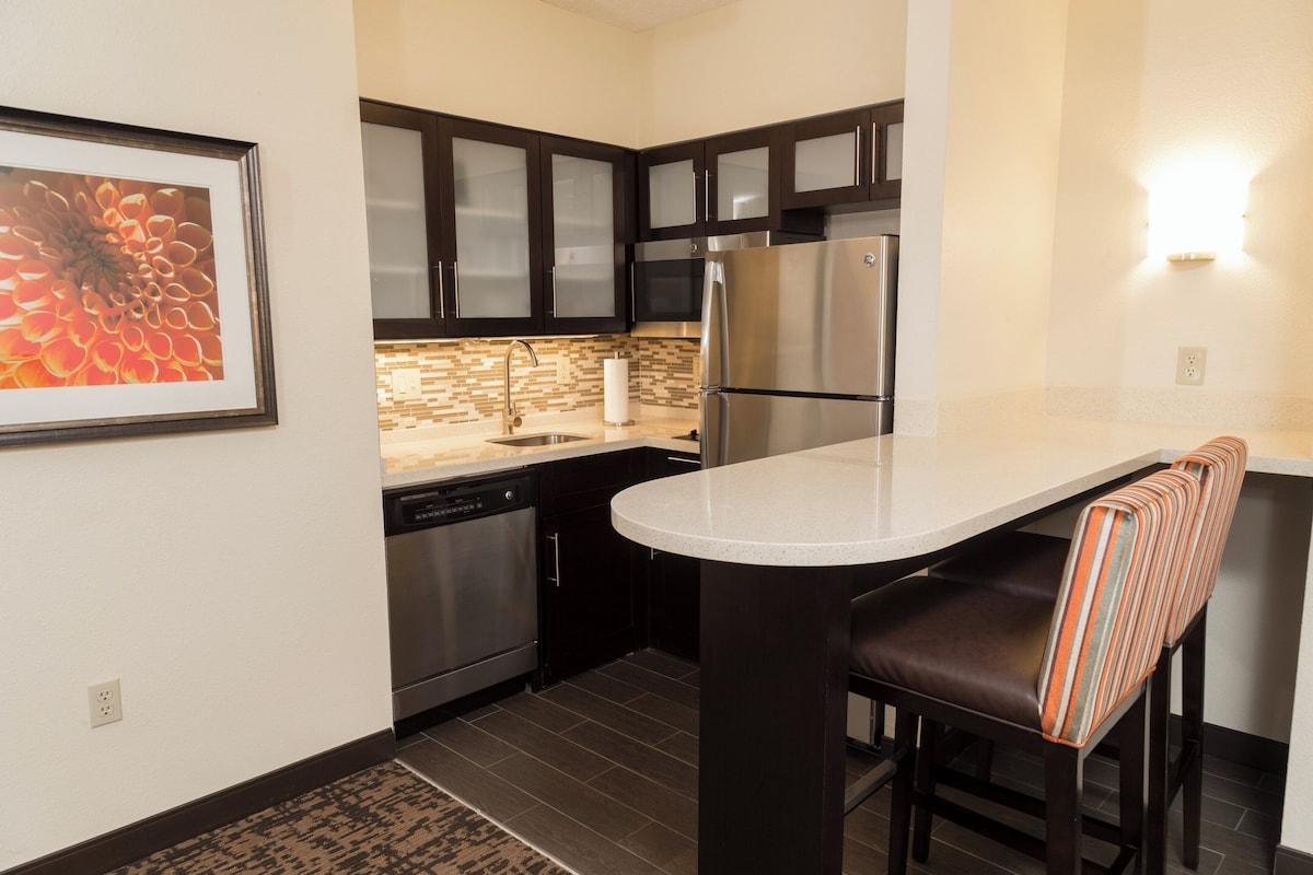A modern kitchen with dark cabinets, stainless steel appliances, and a white countertop.