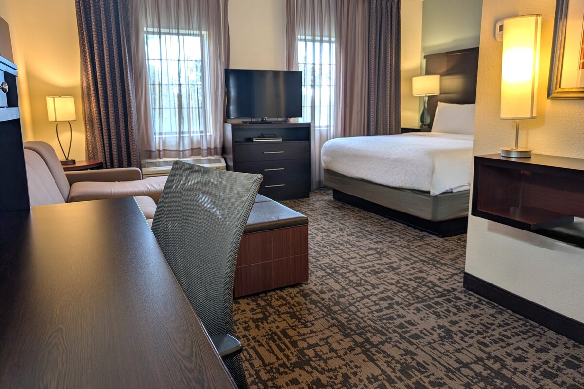 A hotel room with a bed, a desk, a chair, a television, and a dresser.