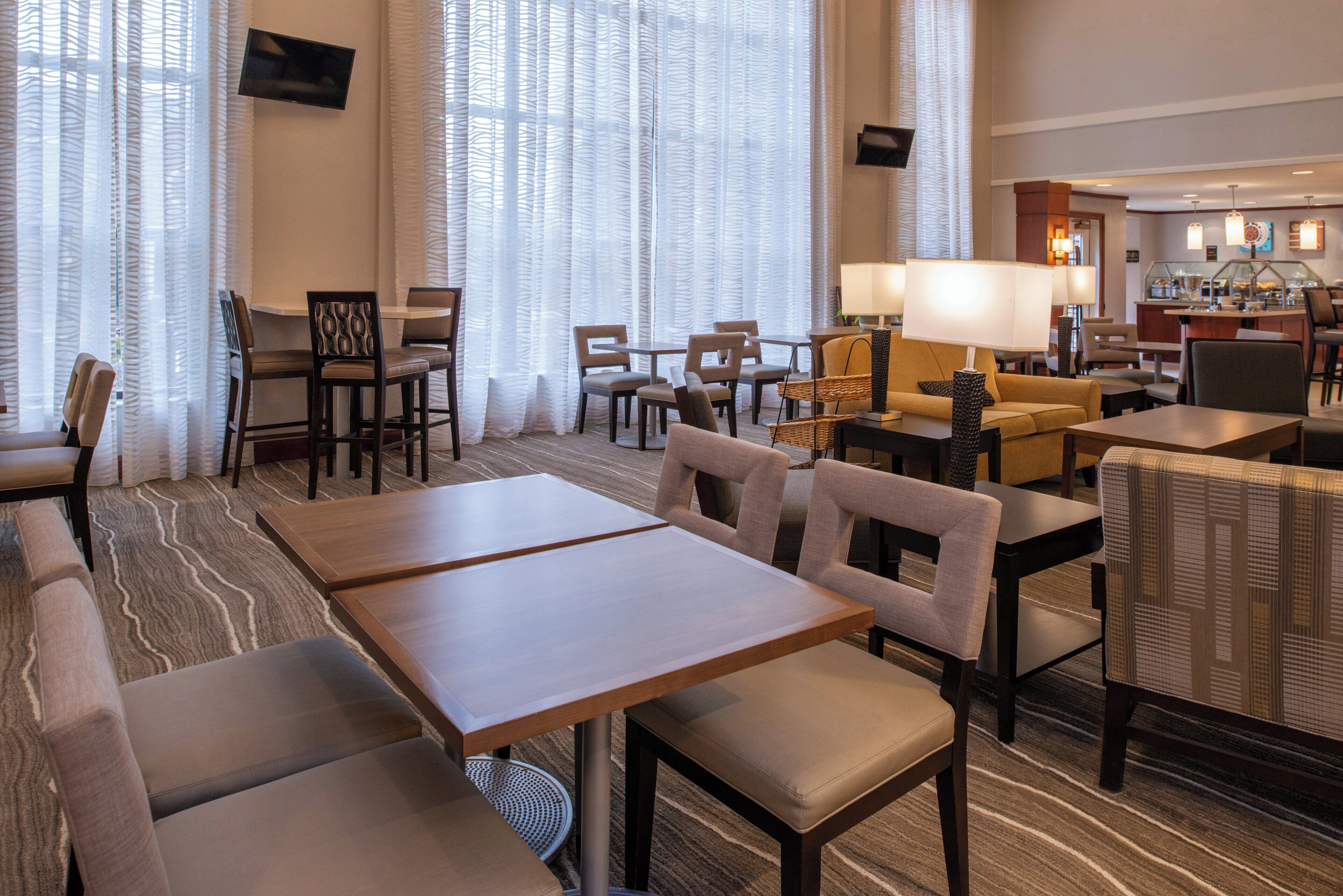 Un hall d’hôtel aménagé avec des espaces salon, un coin café et un téléviseur fixé au mur.