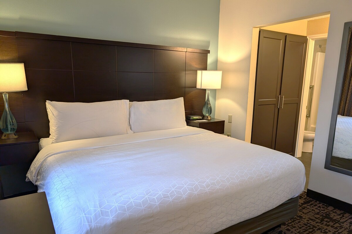A neatly made bed with white linens in a hotel room.