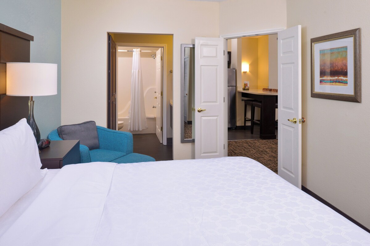 Habitación de hotel con cama, escritorio y baño visible a través de una puerta abierta.