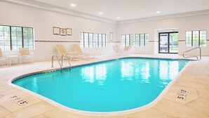A large indoor swimming pool with clear blue water, surrounded by white walls and large windows.