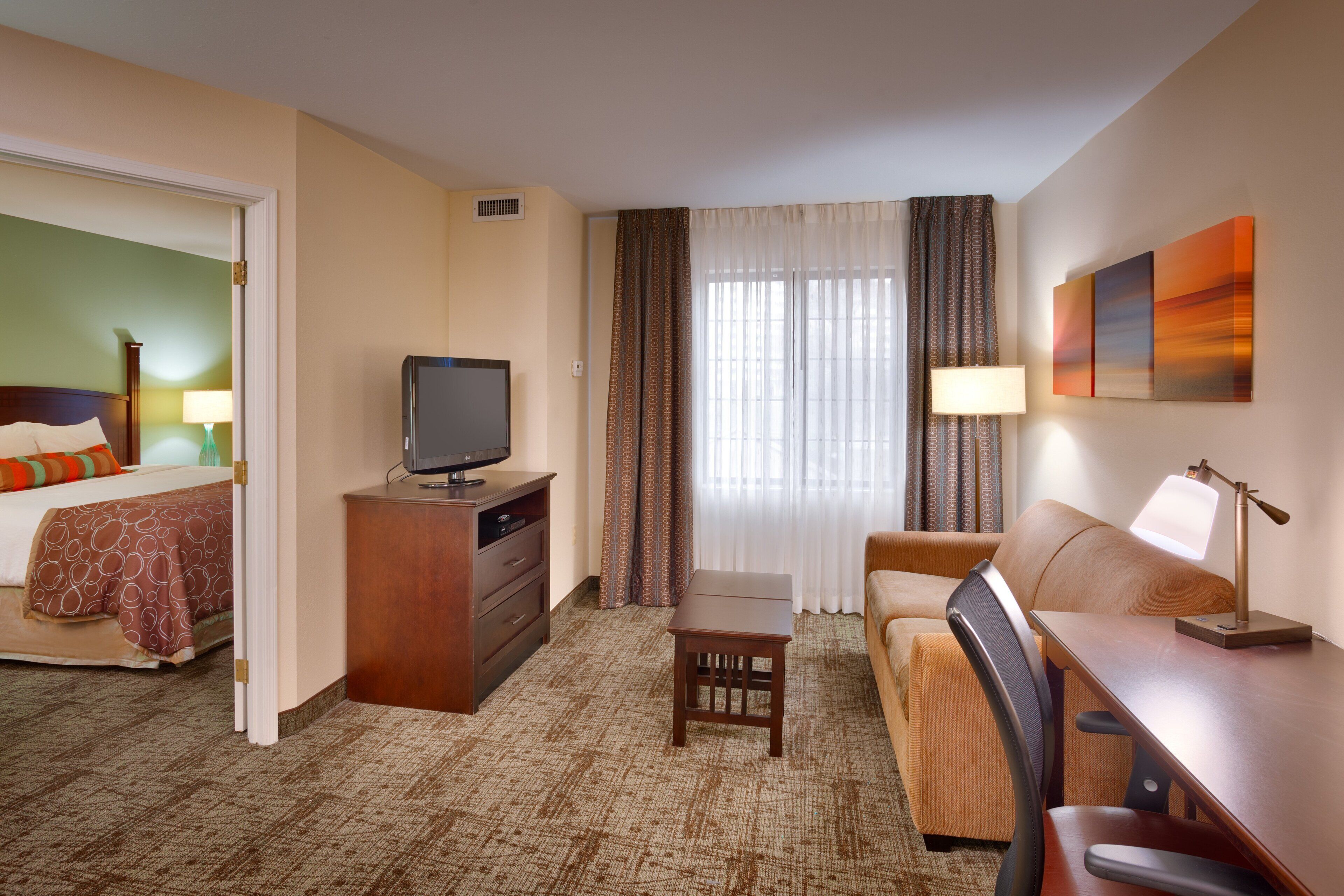 A hotel room with a bed, a desk, a television, a chair, and a window with curtains.