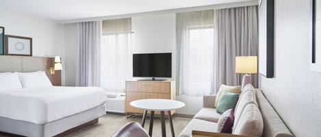 Ett hotellrum med en säng, en tv, en soffa, ett bord och en lampa.