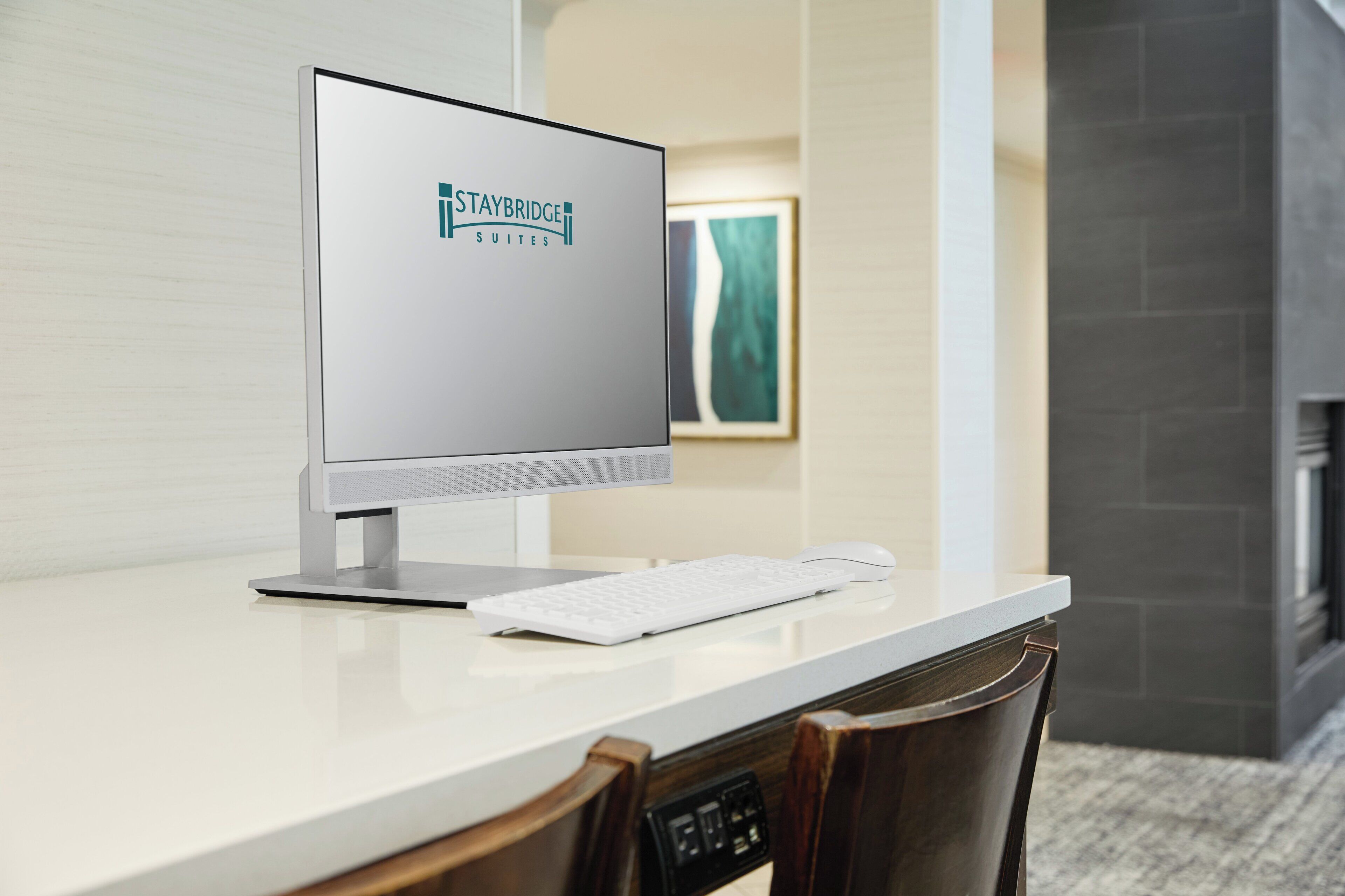 Habitación de hotel moderna con un escritorio blanco, una computadora de escritorio, un teclado y un ratón.