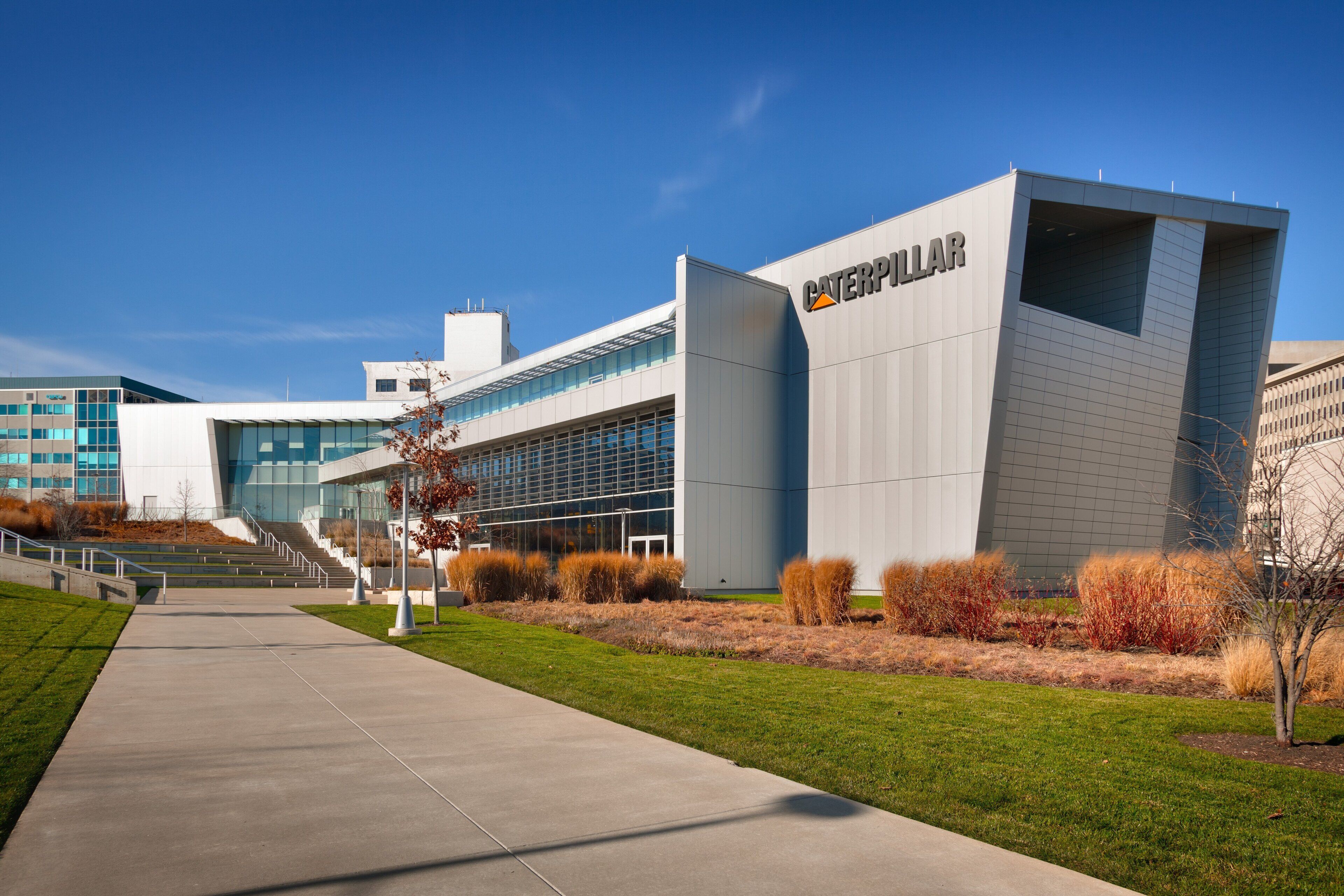 A modern building with a prominent Caterpillar logo, a clear sky, and a well-maintained lawn with pathways leading to the entrance.