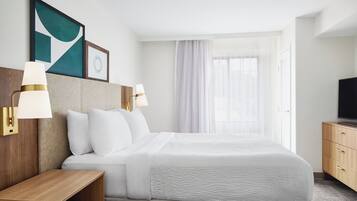 A hotel room with a large bed, two bedside lamps, a wooden nightstand, a TV on a wooden cabinet, and a window with sheer curtains.