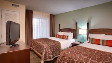 A hotel room with two beds, a television, a desk, and a window with curtains.