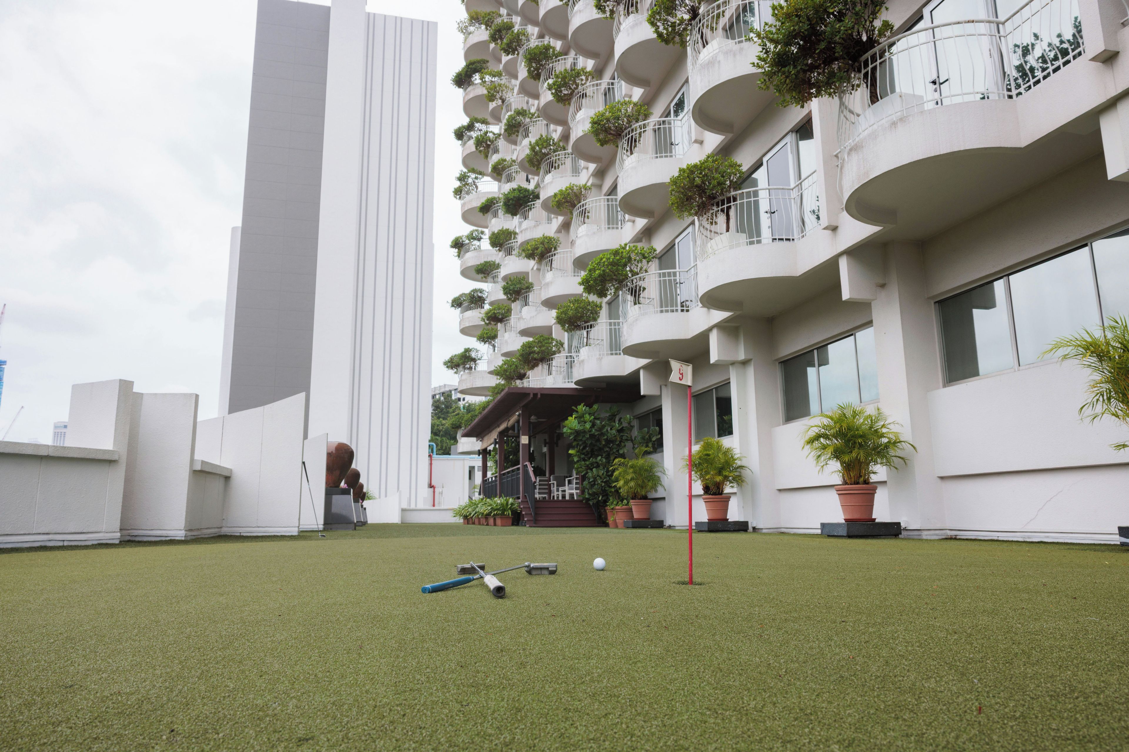 A modern building with multiple balconies, some with plants, and a well-maintained lawn with a flagpole and a golf ball.