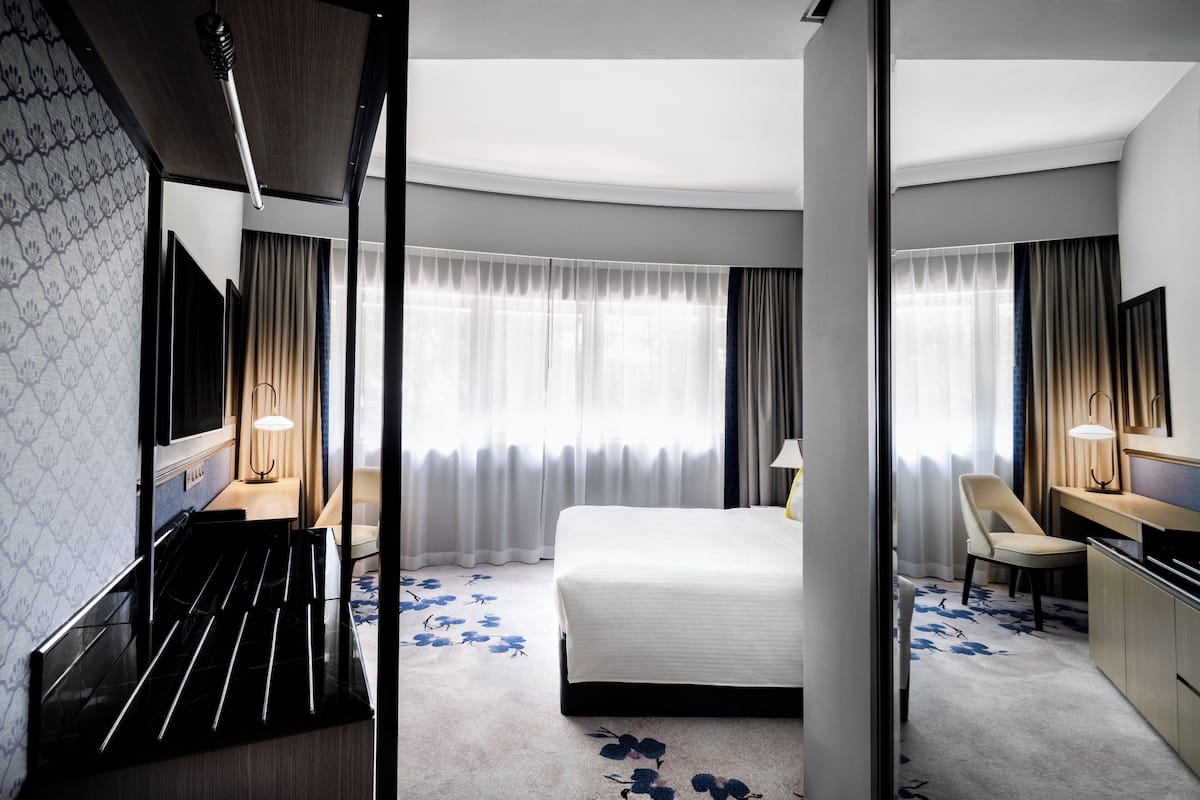 Une chambre d’hôtel avec un lit, un bureau, une chaise, une télévision et une grande fenêtre avec des rideaux.