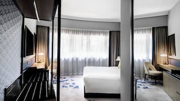 A hotel room with a bed, a desk, a chair, a TV, and a large window with curtains.