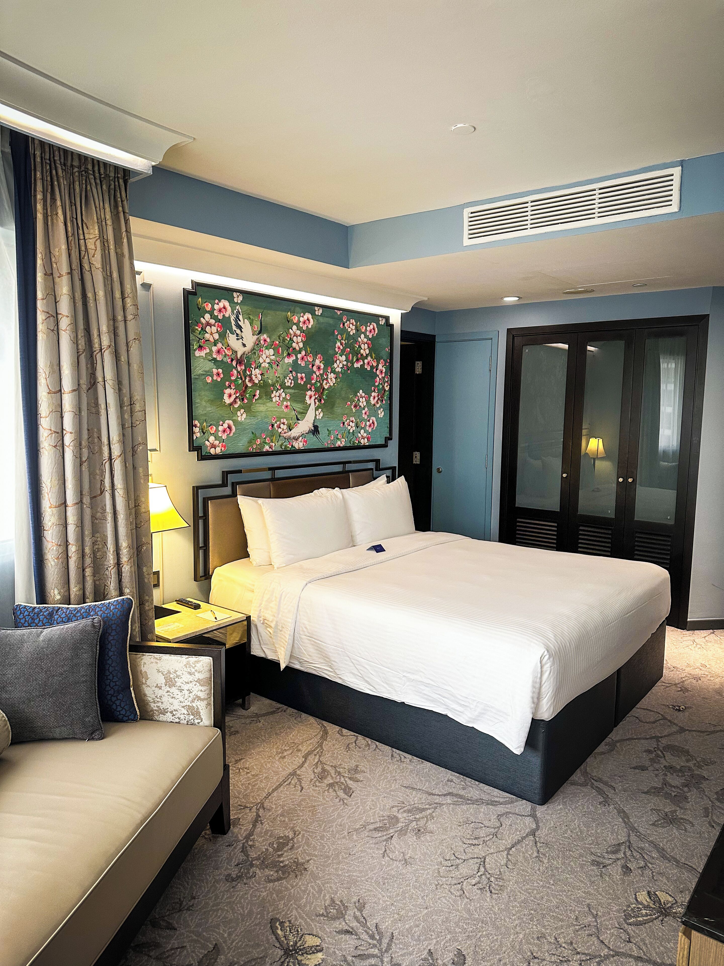 Une chambre d’hôtel avec un grand lit, un canapé, un bureau avec une lampe, un tableau au mur et une armoire.