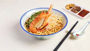Un tazón de fideos con cangrejo, verduras verdes y dos pequeños recipientes de condimentos.