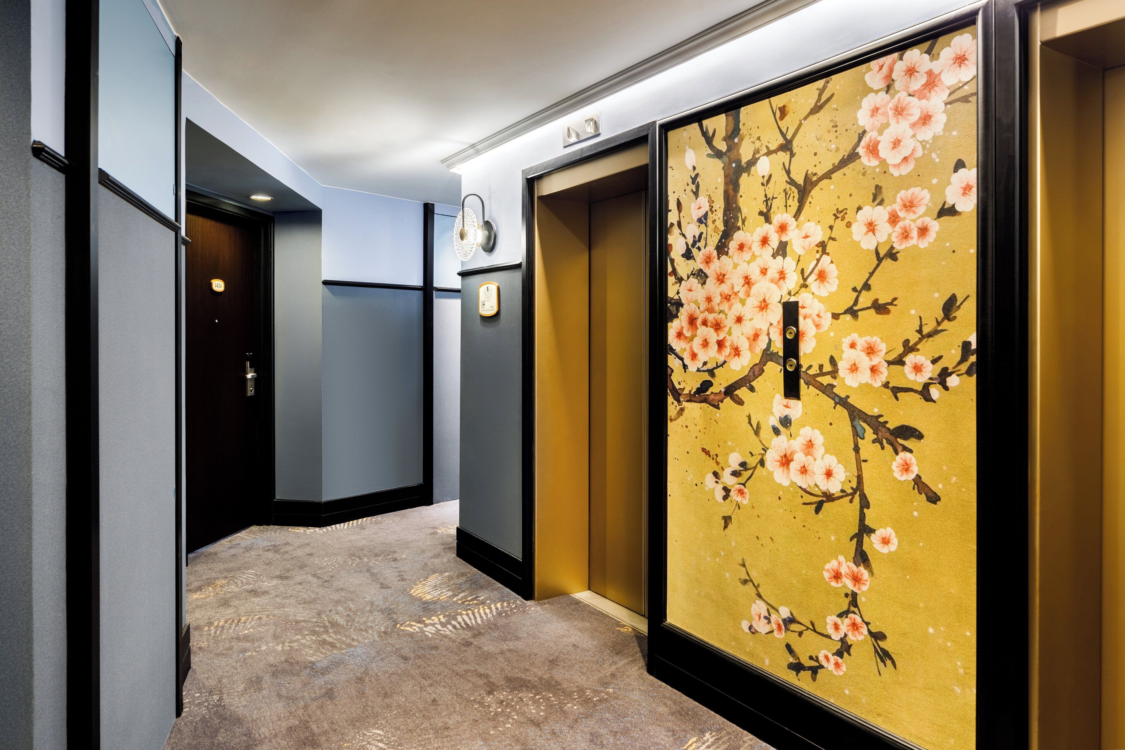 Un couloir doté d’un sol recouvert de moquette, d’un luminaire fixé au mur et d’un paravent japonais traditionnel orné de motifs de fleurs de cerisier.