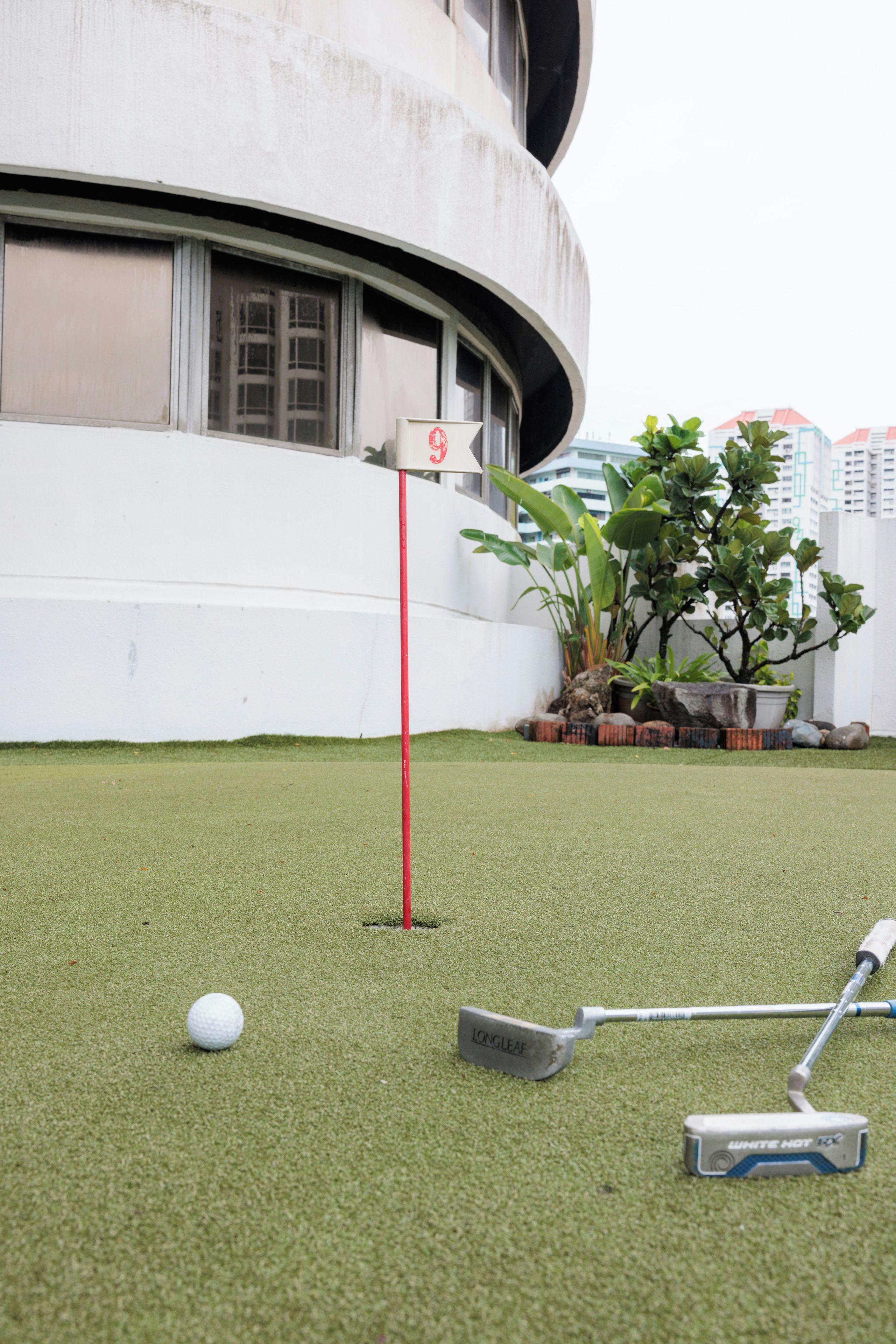 A miniature golf hole with a red flag, a golf ball, and a putter on artificial turf.