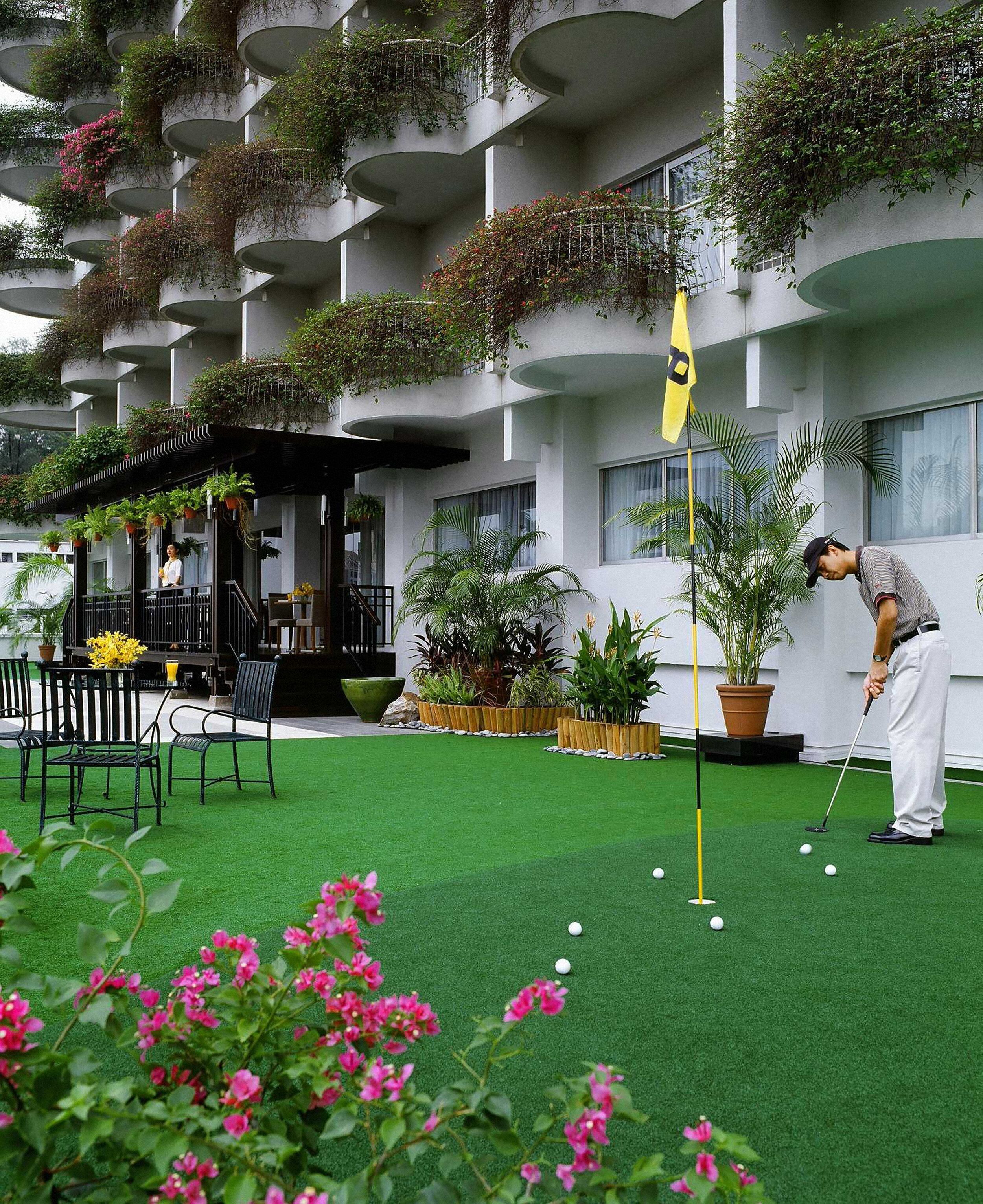 A golf course with a putting green, surrounded by potted plants and a building with balconies.