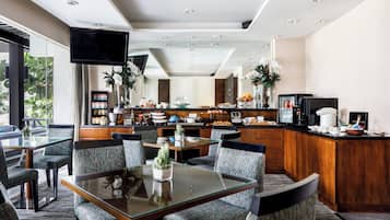 A modern hotel dining area with a glass table, cushioned chairs, and a kitchen in the background.