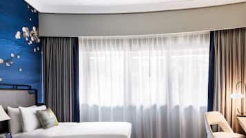 A hotel room with a bed, a chair, a desk, and a lamp.