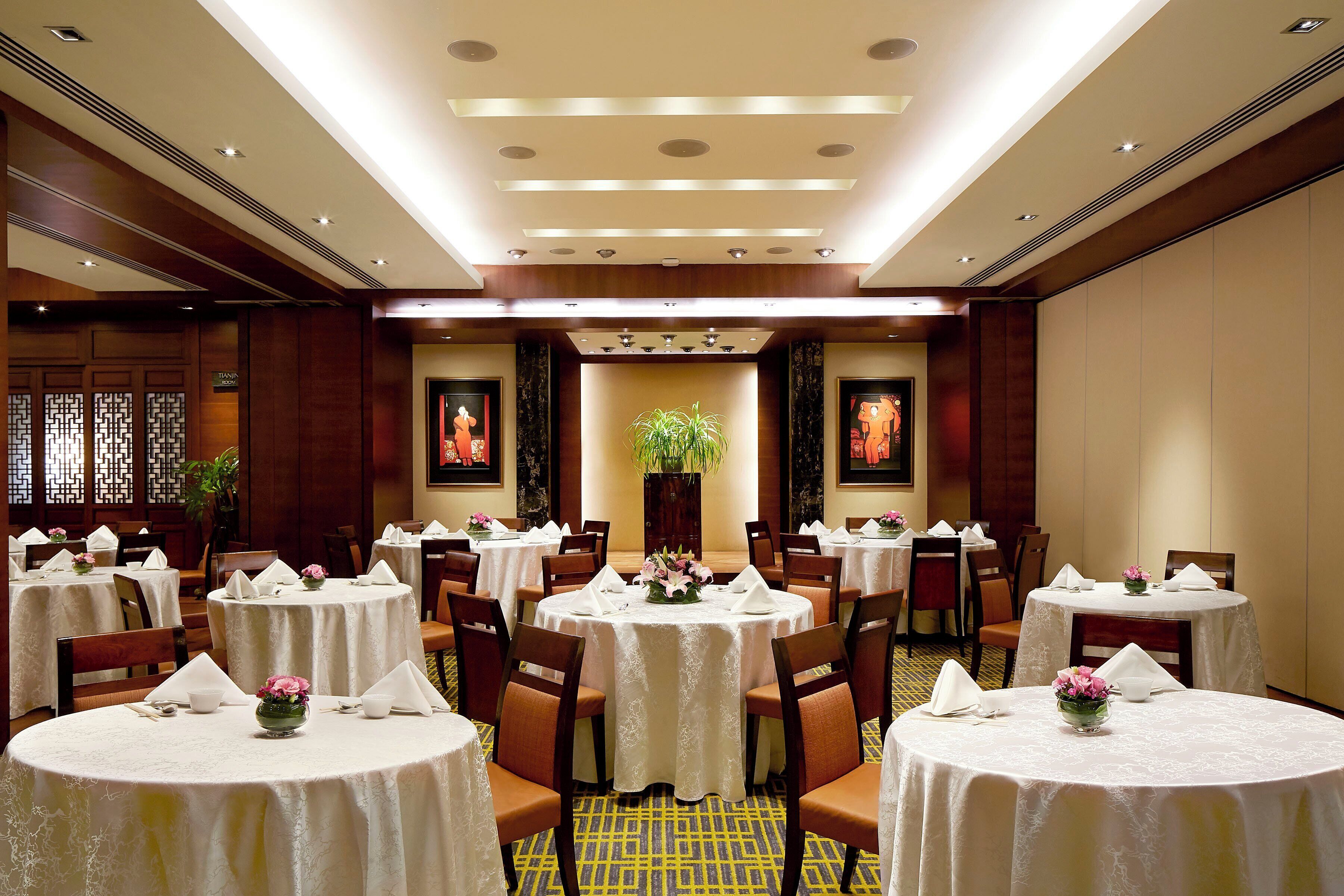 Un comedor de hotel con mesas redondas, sillas y manteles blancos.