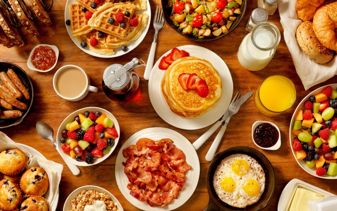 A breakfast spread with waffles, bacon, eggs, and various fruits.