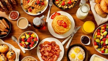 A breakfast spread with waffles, bacon, eggs, and various fruits.