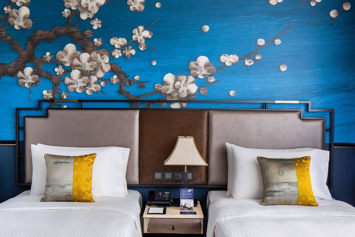 Une chambre d’hôtel avec deux lits, une table de chevet, une lampe et une fresque murale.