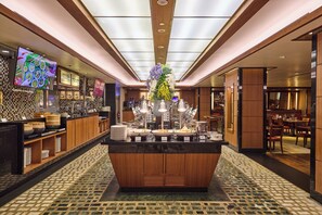 A hotel lobby with a central buffet area, a television screen, and a floral centerpiece. - Copthorne King's Hotel Singapore (Singapore)