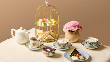 Una mesa dispuesta con un juego de té, tazas, una bandeja de sándwiches, un florero con flores y una jaula decorativa.