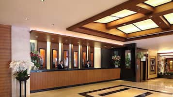 A hotel reception area with a wooden reception desk, multiple receptionists, and a large, geometric patterned floor.