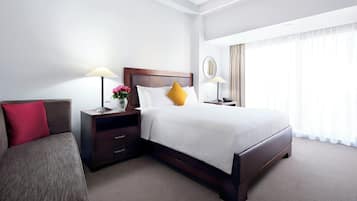 A hotel room with a large bed, a bedside table with a lamp, a nightstand with a lamp, a red pillow, and a brown sofa.