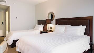 A hotel room with two beds, a bedside table with a lamp, a mirror, and a chair.