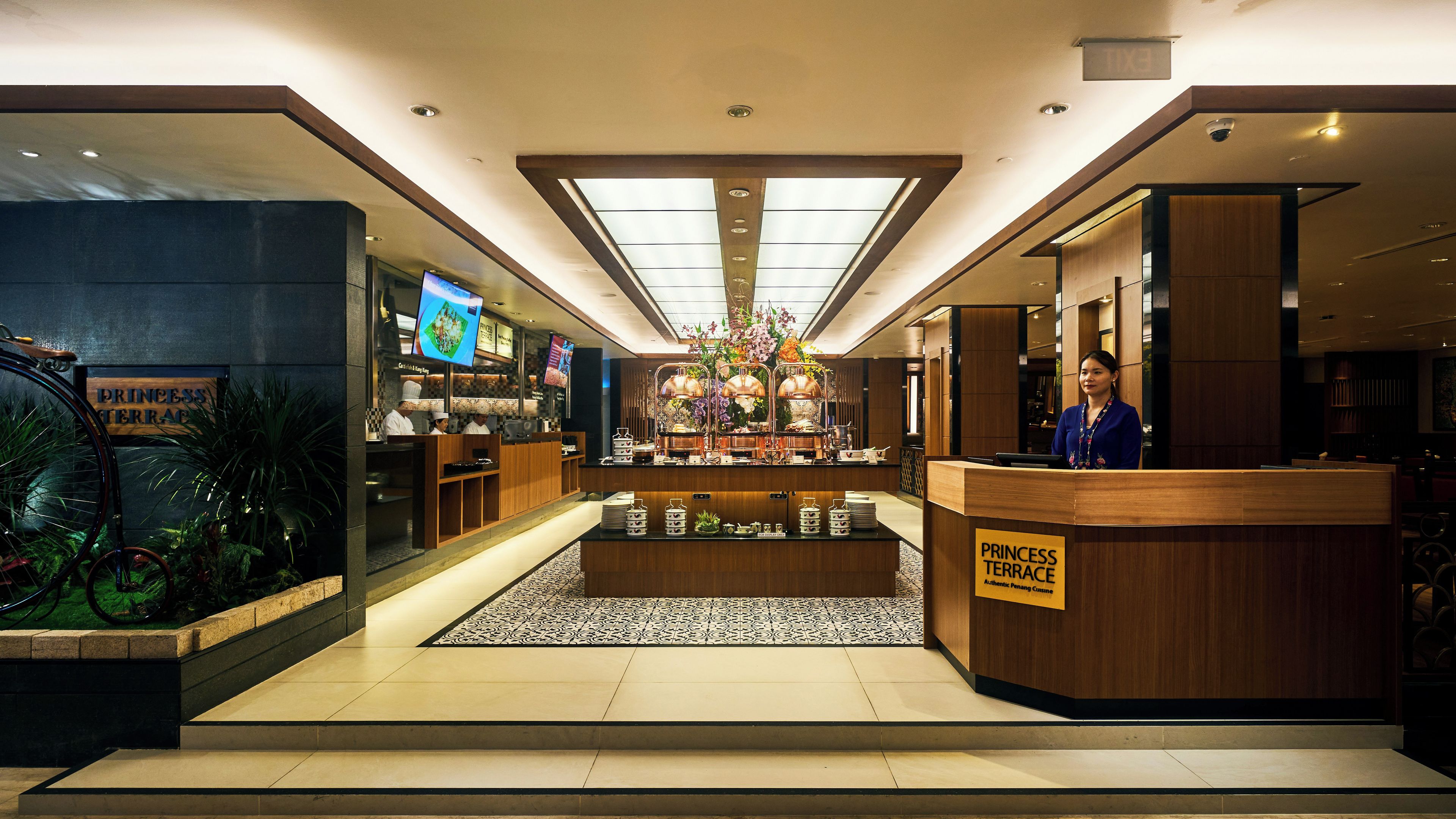 A hotel lobby with a reception desk, a digital screen, and a floral centerpiece.