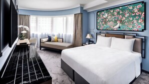 A hotel room with a large bed, a sofa, a desk with a flat-screen TV, and a large floral artwork on the wall.