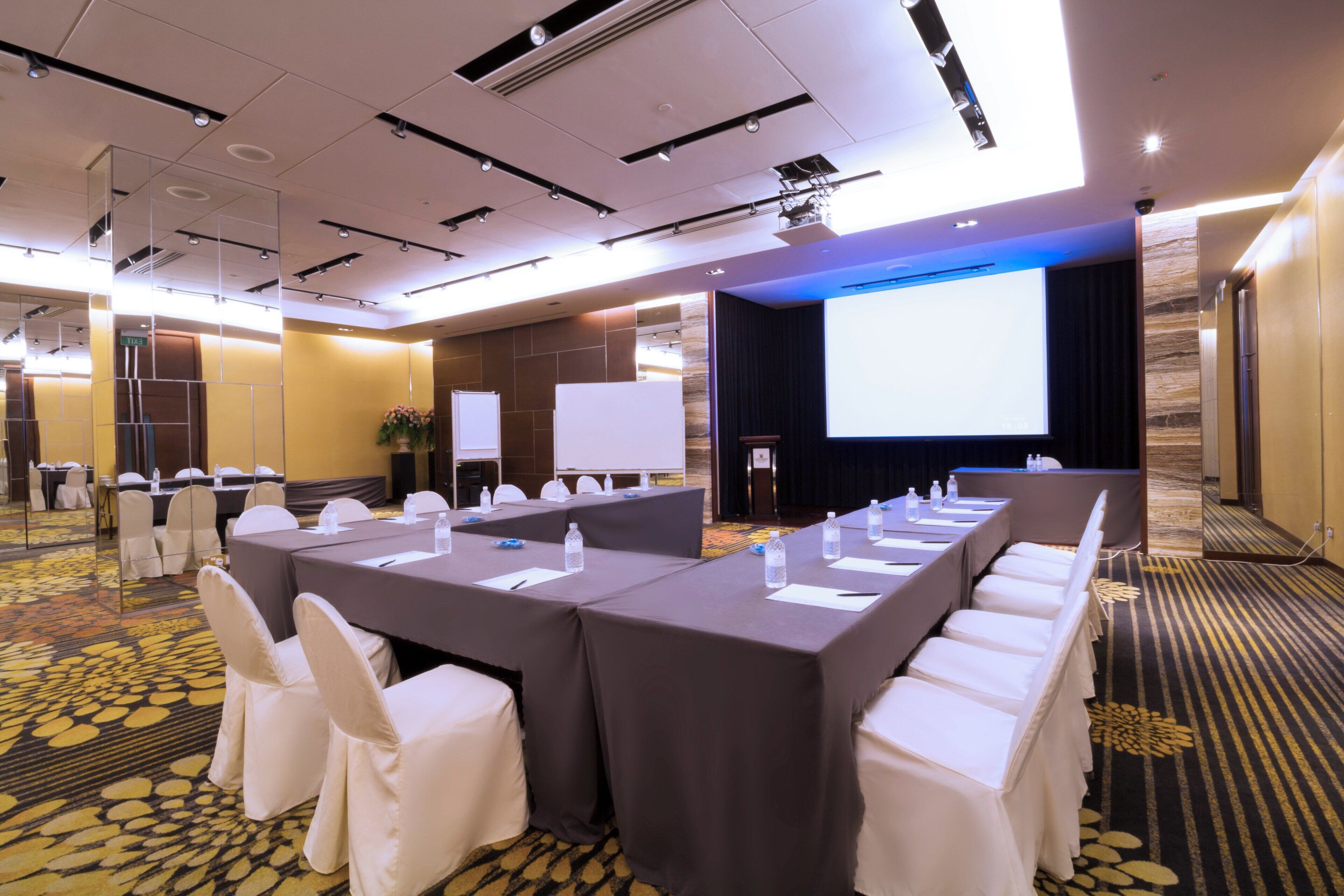 A conference room with long tables, white chairs, and a large screen for presentations.
