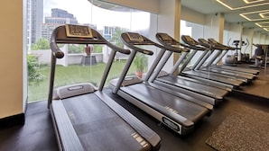 A gym with treadmills aligned in rows, large windows offering a view of buildings and greenery outside.