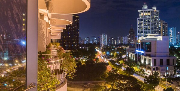 A nighttime cityscape with modern buildings, a well-lit balcony, and a view of the urban area.