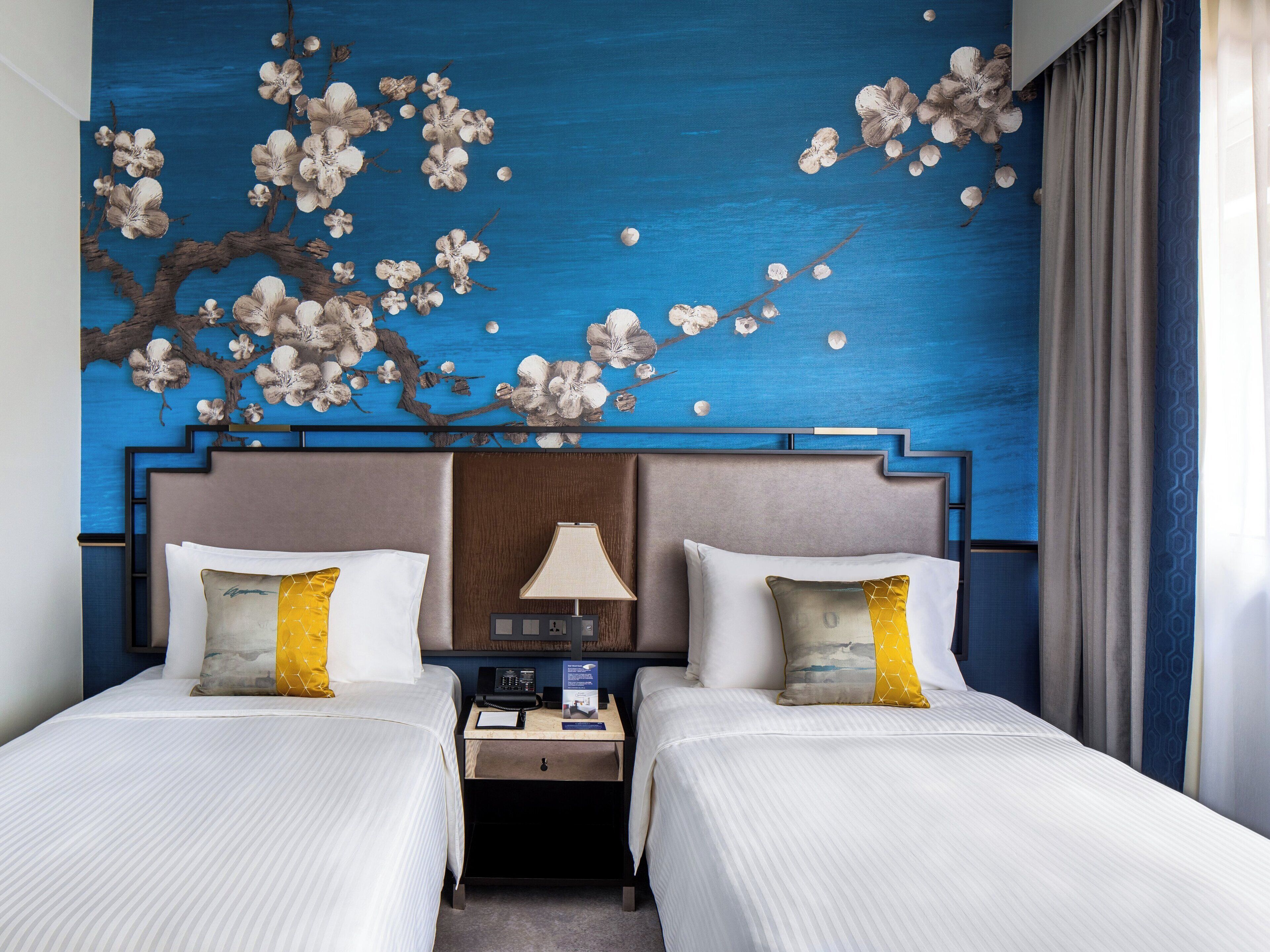 A hotel room with two beds, a nightstand with a lamp, and a wall mural of flowers.