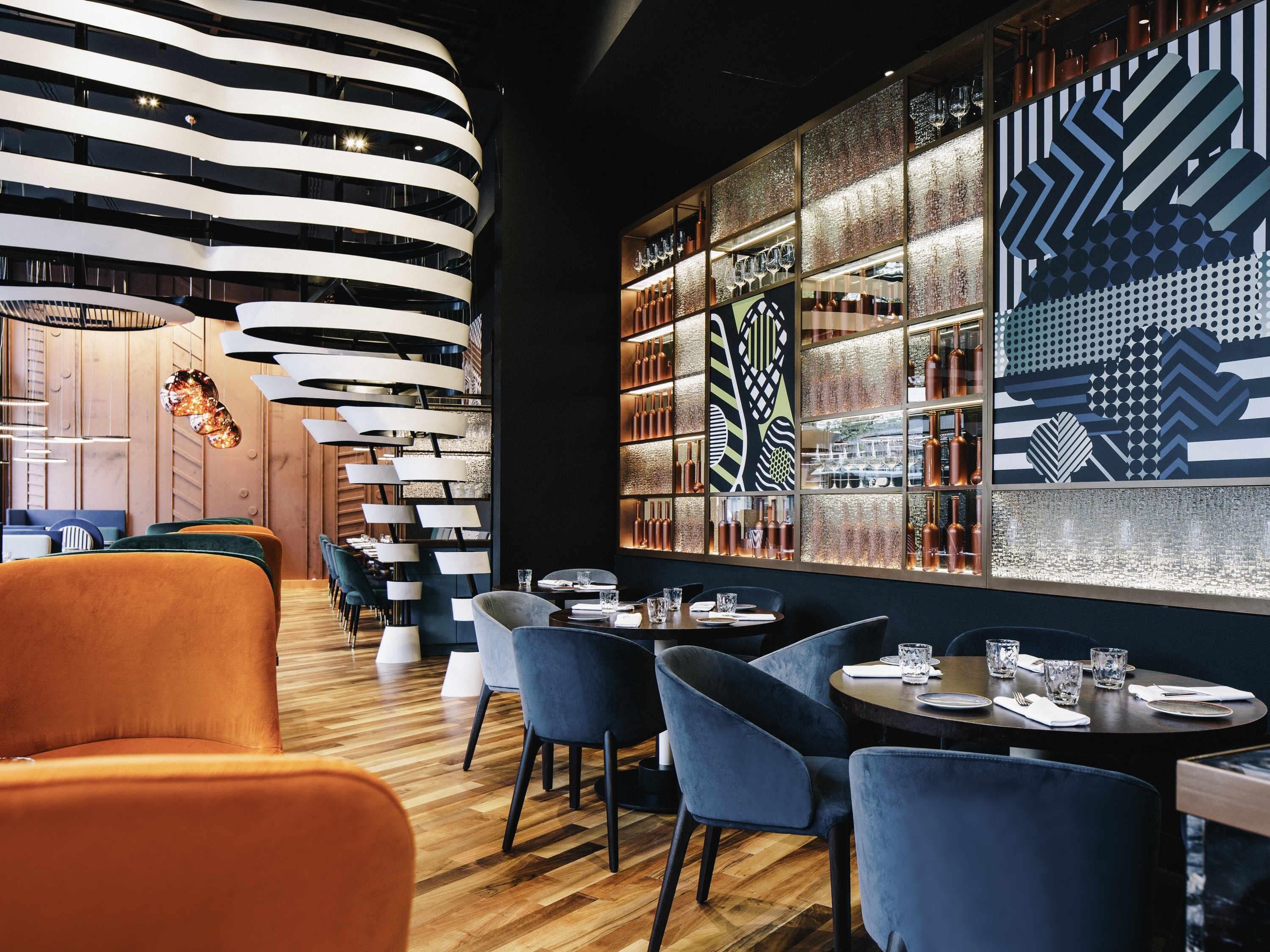 Un interior de restaurante moderno con suelo de madera, sillas tapizadas en azul y una lámpara de techo curva.