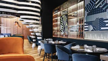 Un interior de restaurante moderno con suelo de madera, sillas tapizadas en azul y una lámpara de techo curva.