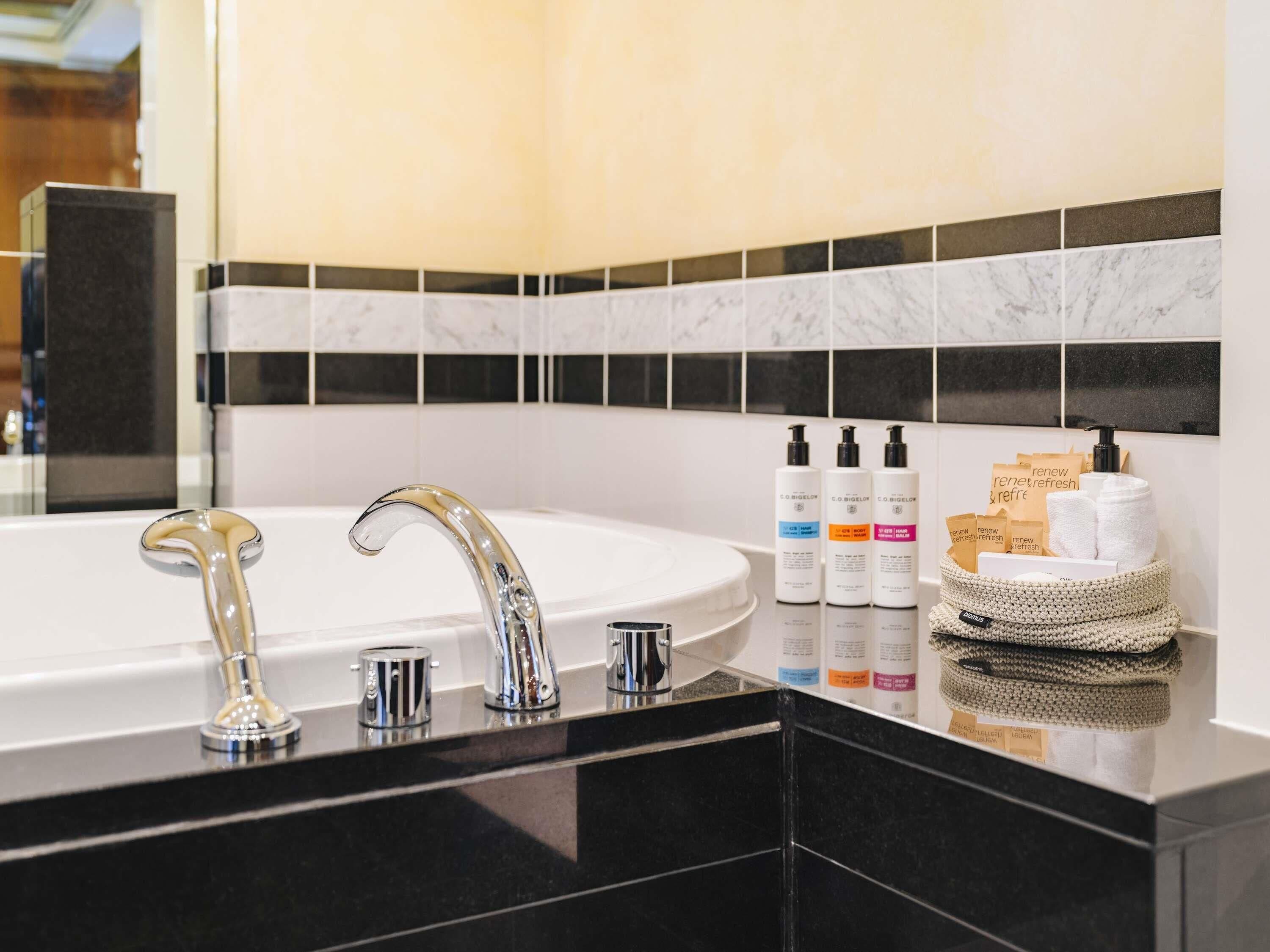 A bathroom with a white bathtub, two chrome faucets, and a black countertop.