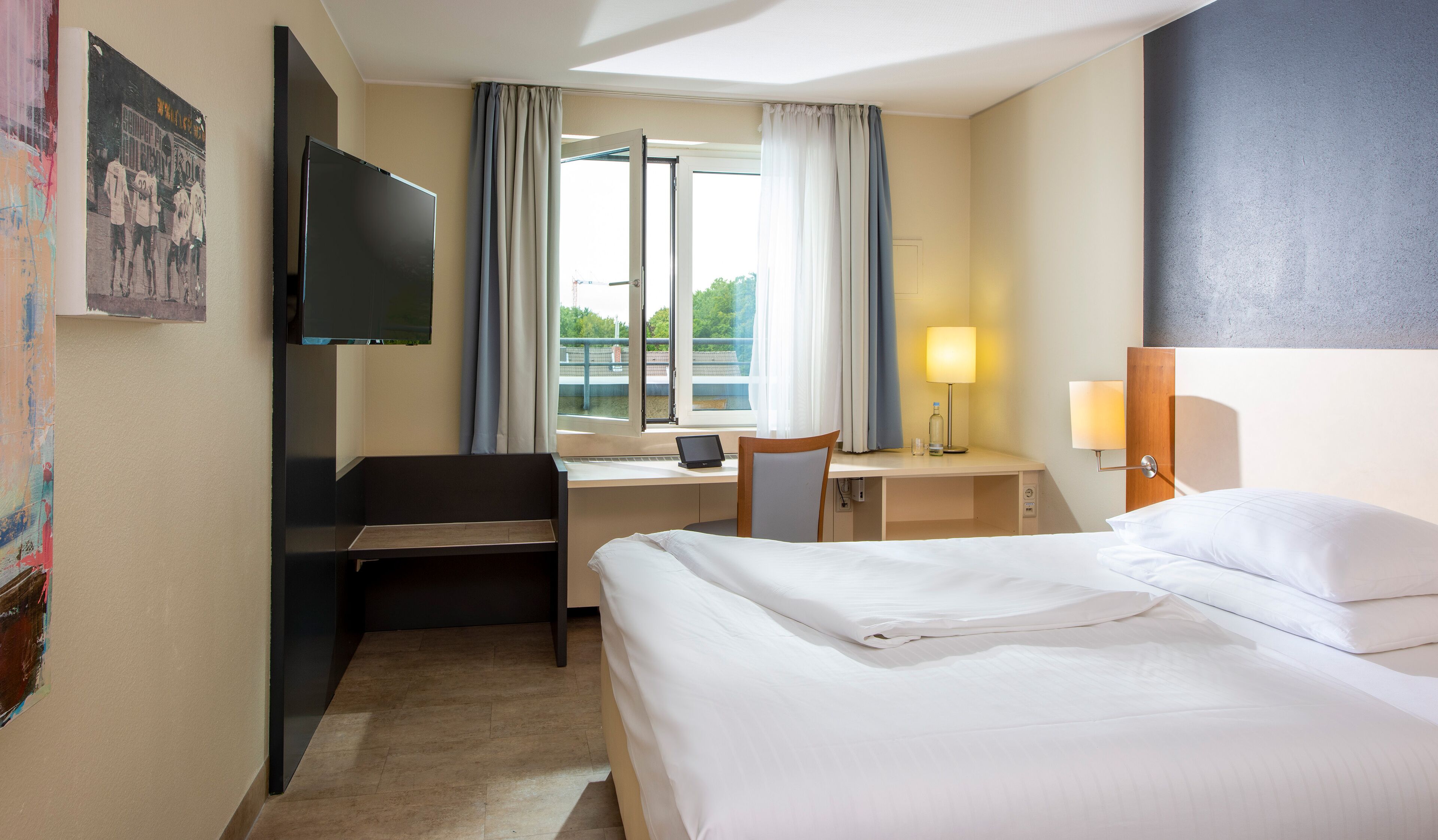 Ein Hotelzimmer mit Bett, Schreibtisch, Stuhl, Fernseher und einem Fenster mit Vorhängen.