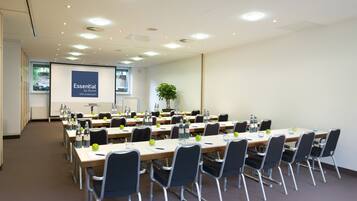 A conference room with multiple tables, chairs, and a projector screen displaying "Essential by Dorint".