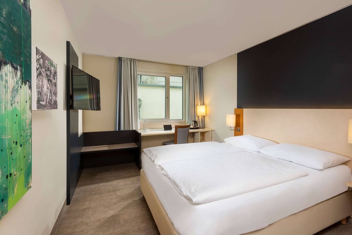 A hotel room with a bed, desk, chair, and a TV mounted on the wall.