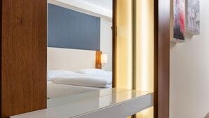 Una moderna camera d'hotel con un grande specchio, un letto con lenzuola bianche, una testiera in legno e una lampada a parete.